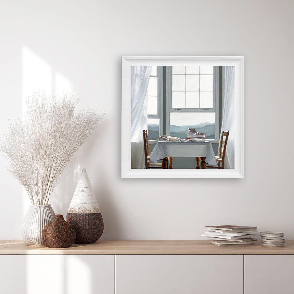 Framed print of a restful cat lying on a table with books.