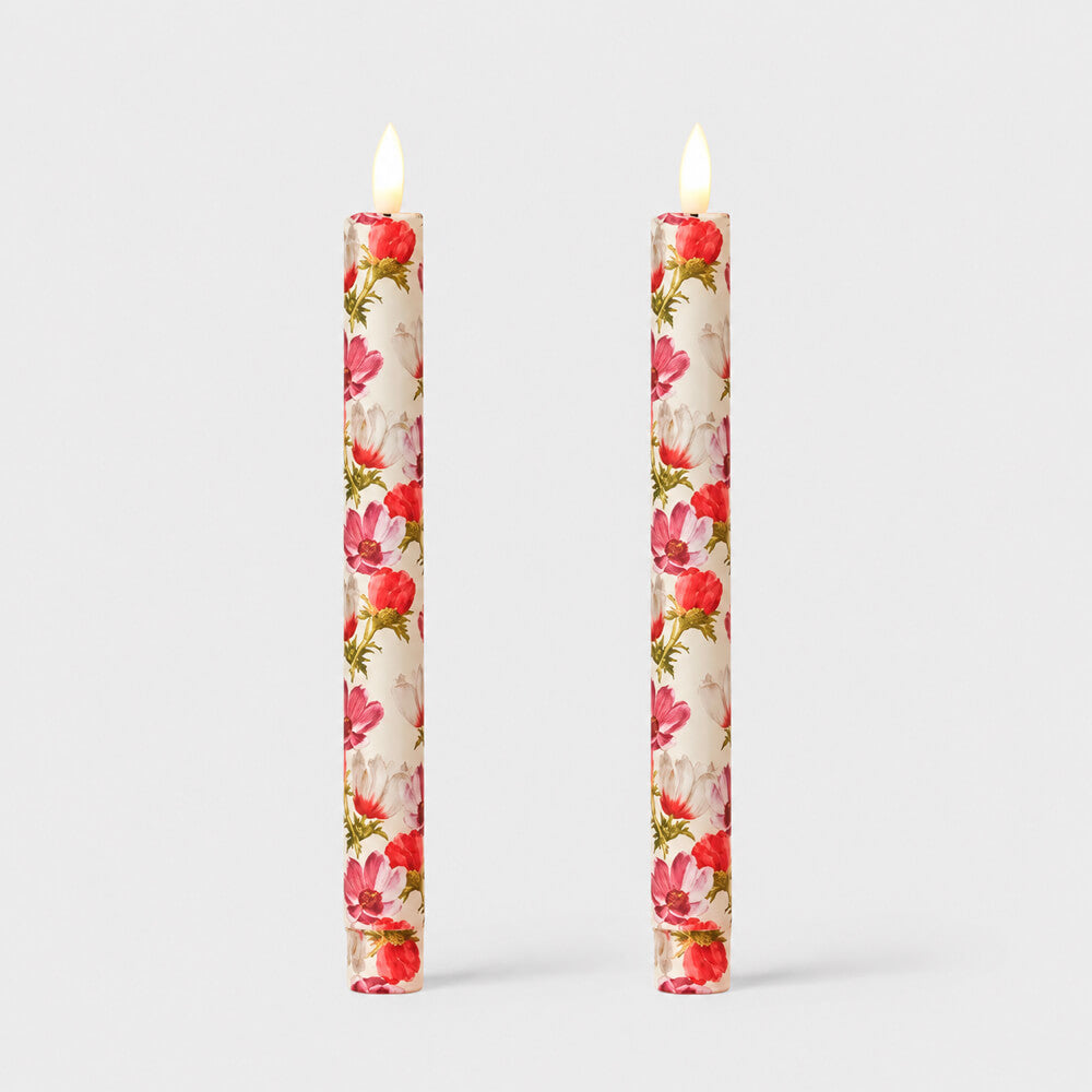 Two tall taper fabric wrapped LED candles with a pink and red floral pattern, shown lit against a light grey studio background.