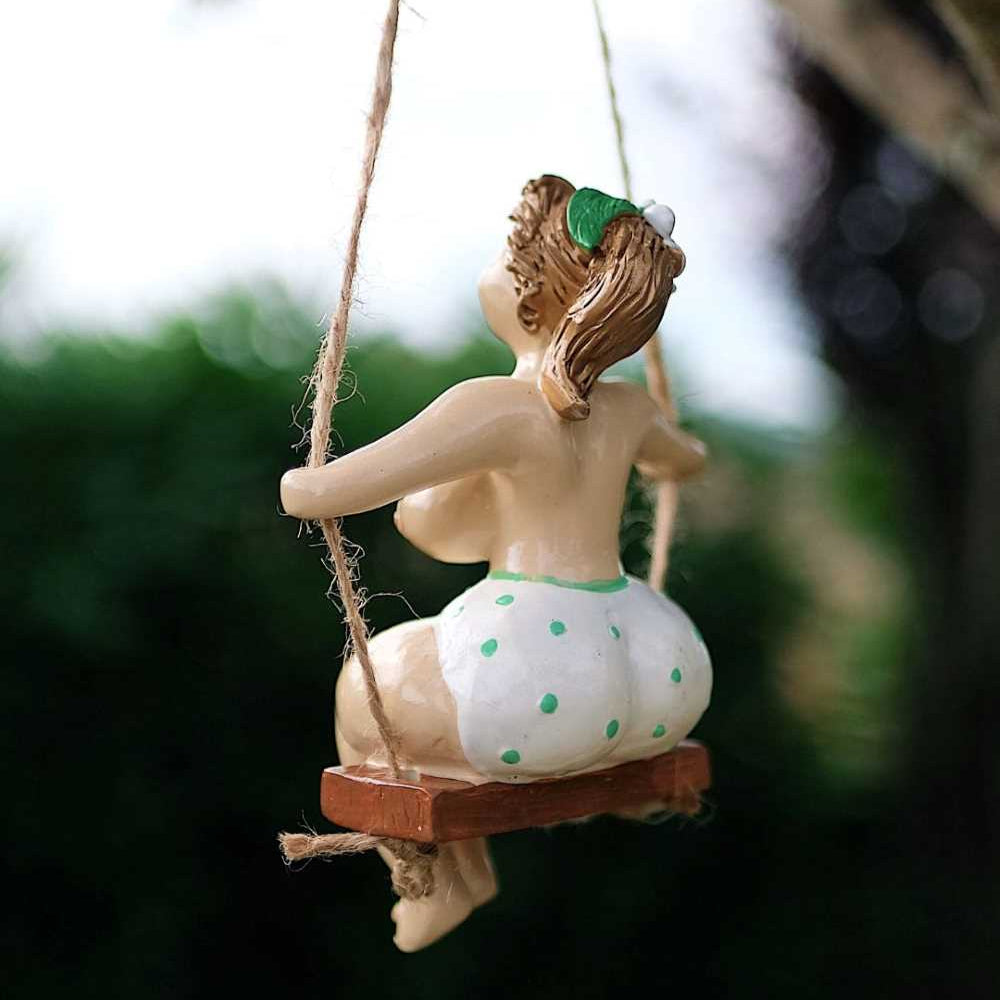 Decorative figurine of a woman on a swing with a green headband against a blurred natural background