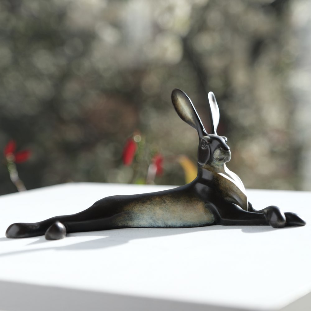 Bronze statue of a hare on a white surface with a blurred natural background