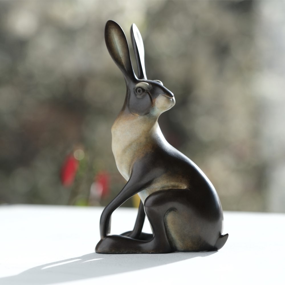 Bronze hare sculpture on a reflective surface with a blurred natural background