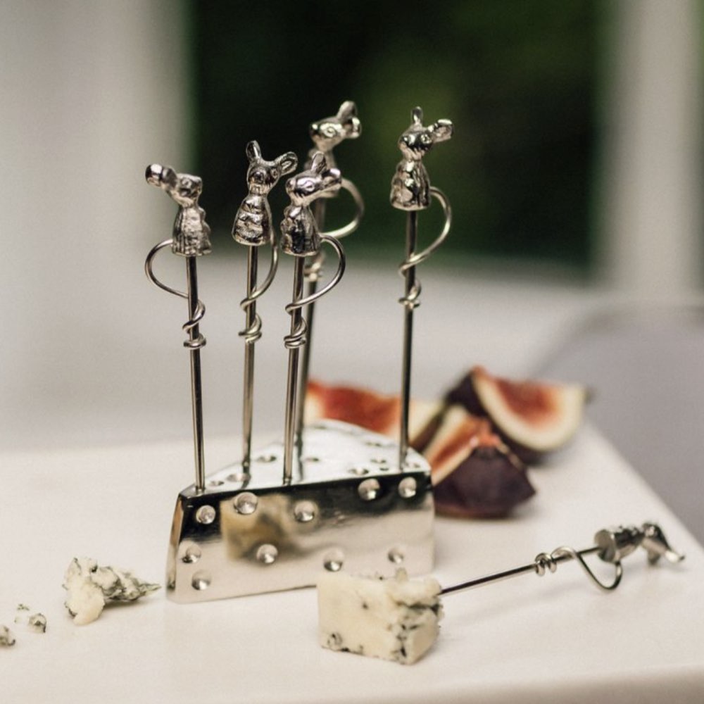 Set of silver cheese picks shaped like mice on a stand with figs and cheese in the background.