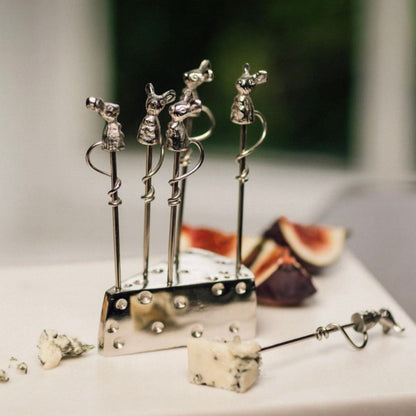 Set of silver cheese picks shaped like mice on a stand with figs and cheese in the background.