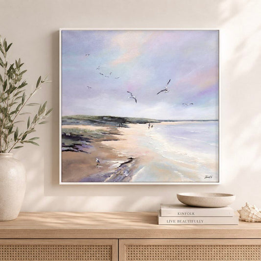 Framed beach painting on a wall above a wooden console table with decorative items.