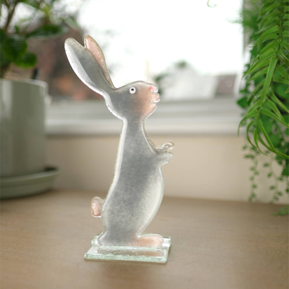Glass rabbit figurine on a table with plants in the background