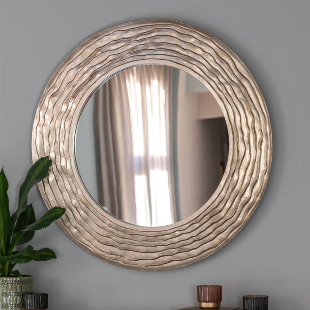 Round decorative mirror with wavy border on a gray wall