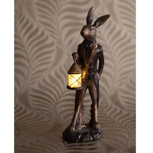 Bronze rabbit statue holding a lit lantern against a textured wall.