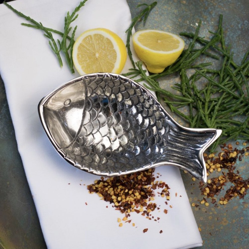 Silver fish-shaped dish with lemons and herbs on a stone surface