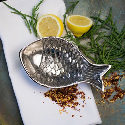 Silver fish-shaped dish with lemons and herbs on a stone surface
