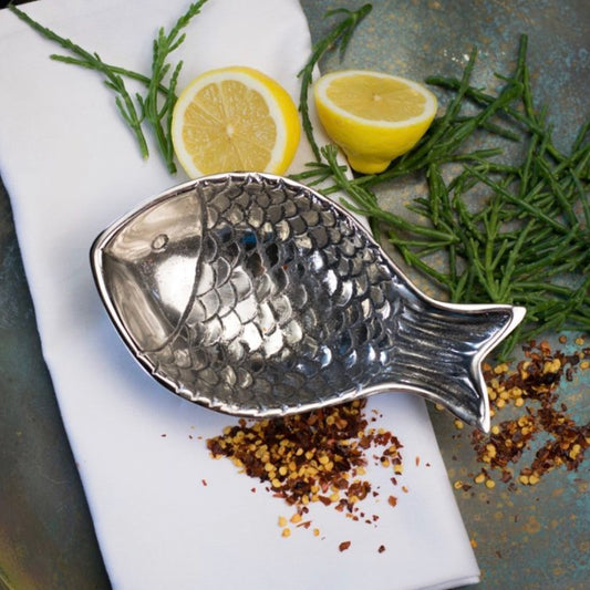 Silver fish-shaped dish with lemons and herbs on a stone surface