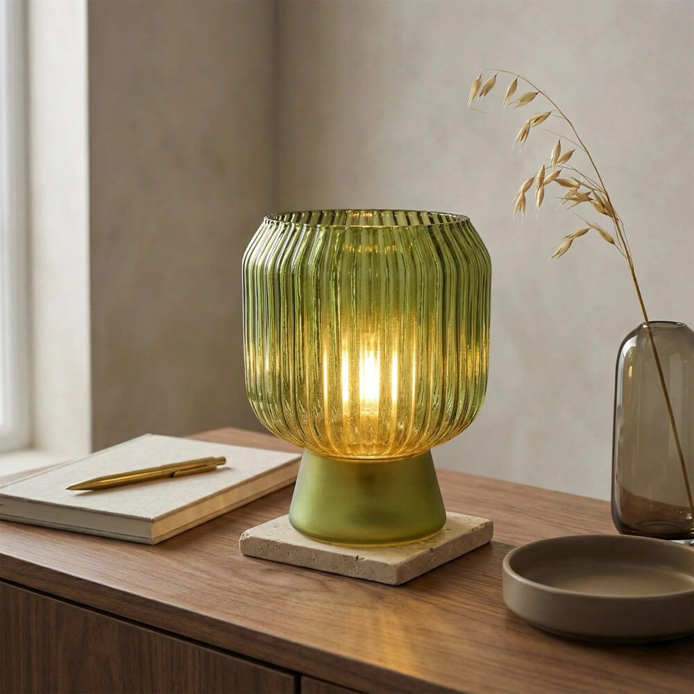 Green glass table lamp on a wooden surface with a notebook and pen.