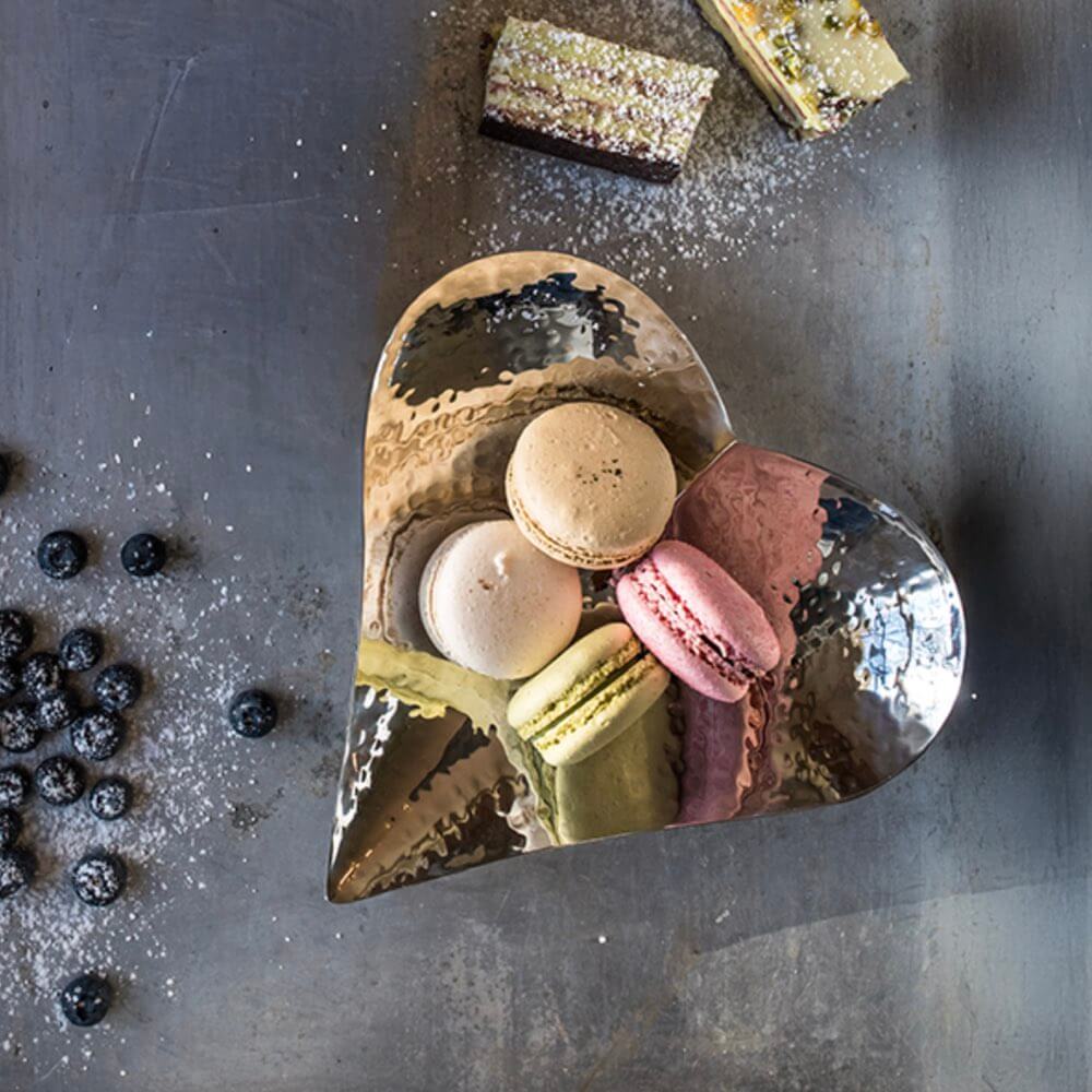 Heart-shaped metal dish with macarons on a textured surface