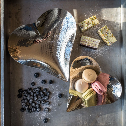 Heart-shaped metal dish with macarons and berries on a metallic surface