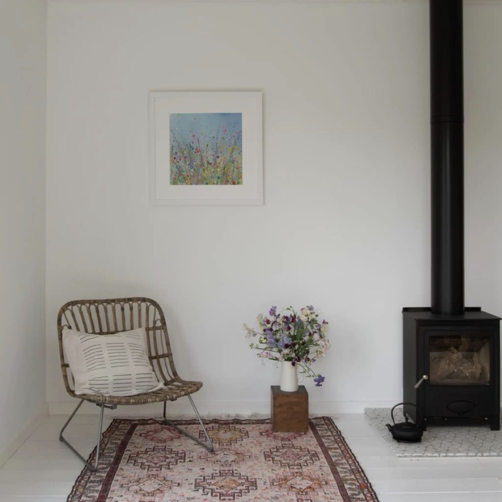 Snug living room with a wicker chair, floral arrangement, and wood stove.