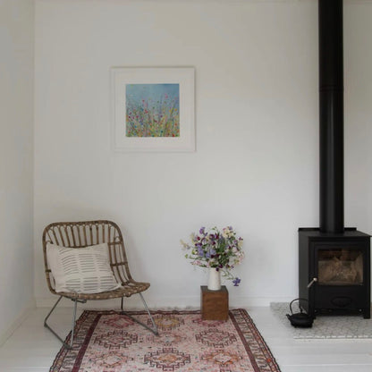Snug living room with a wicker chair, floral arrangement, and wood stove.