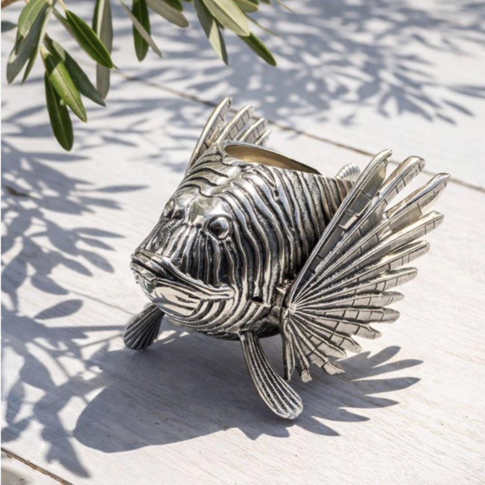Silver fish sculpture on a white surface with green leaves in the background