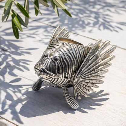 Silver fish sculpture on a white surface with green leaves in the background