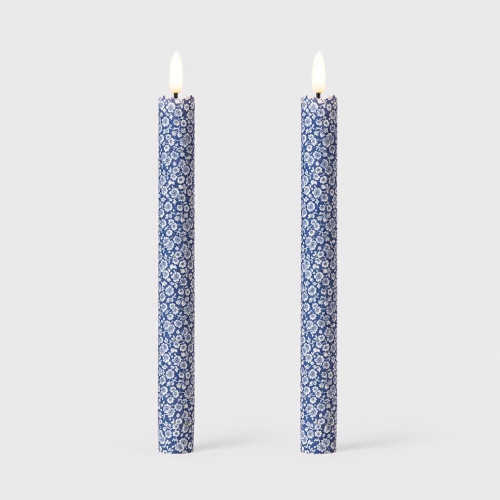 Two blue and white patterned taper LED candles with flames on, standing upright against a light grey background.