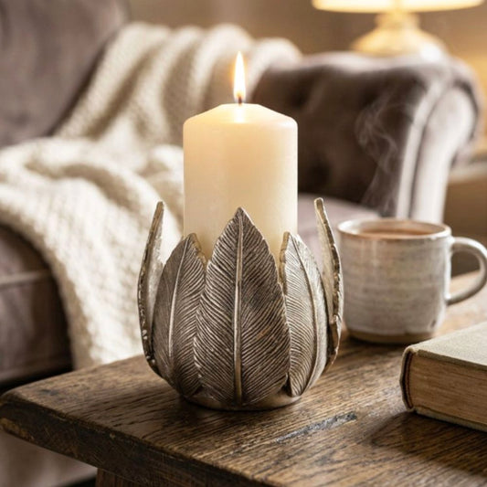 Candle in a leaf-shaped holder on a wooden table with a cup and book in the background.