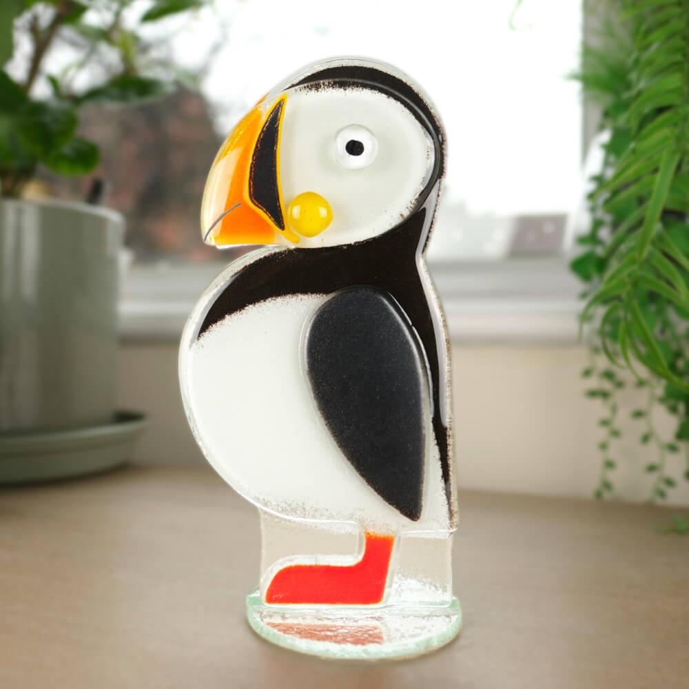 Glass sculpture of a puffin on a table with plants in the background