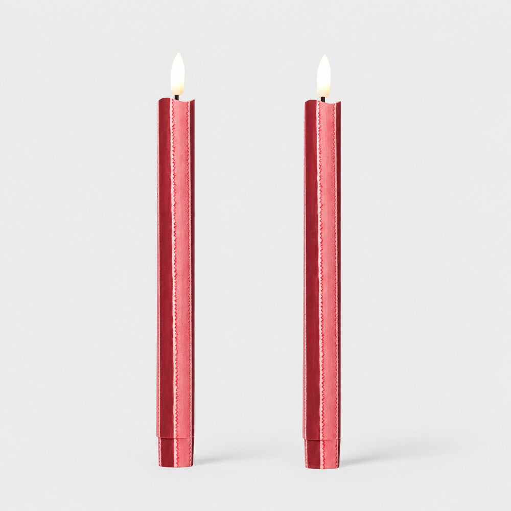 Two tall, slender, red and pink striped fabric wrapped LED candles with lit flame tips, upright against a clean light grey background.