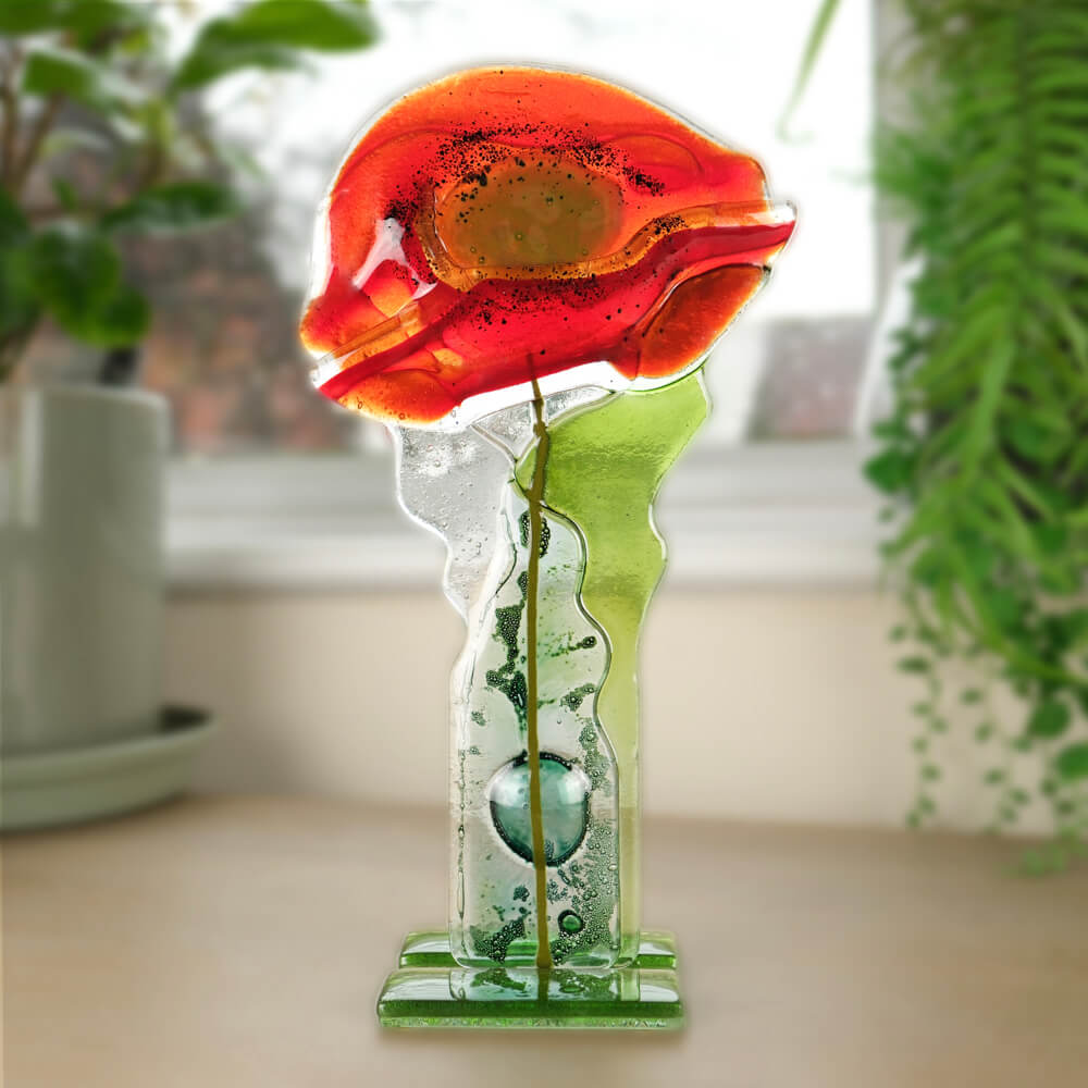 Decorative glass sculpture of a flower on a table with plants in the background