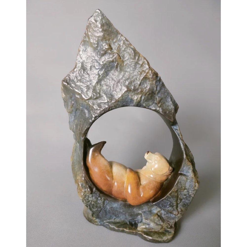 Bronze sculpture with a circular opening displaying a sleeping bear.