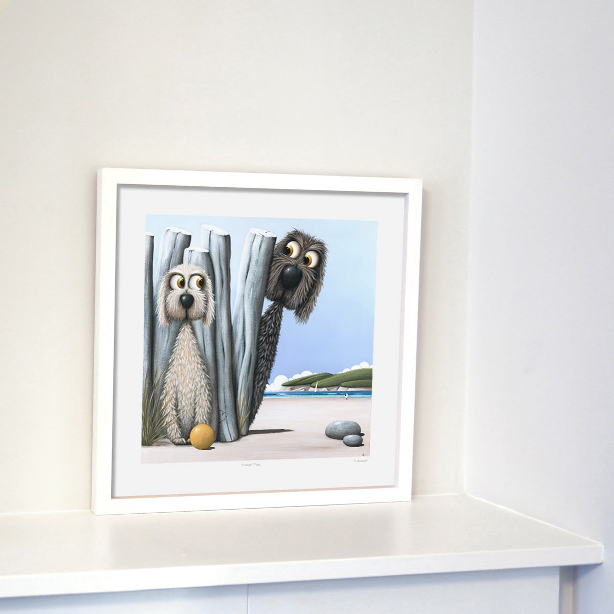 A framed print featuring two cartoon dogs playing hide and seek on a beach, with one dog hiding behind a rock and the other looking on.