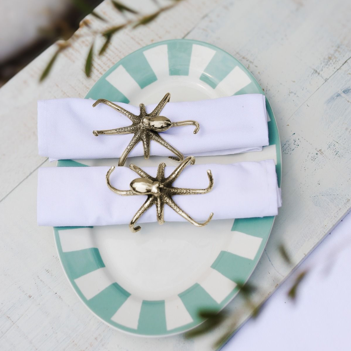 Gold octopus napkin rings on white napkins with a decorative plate in the background