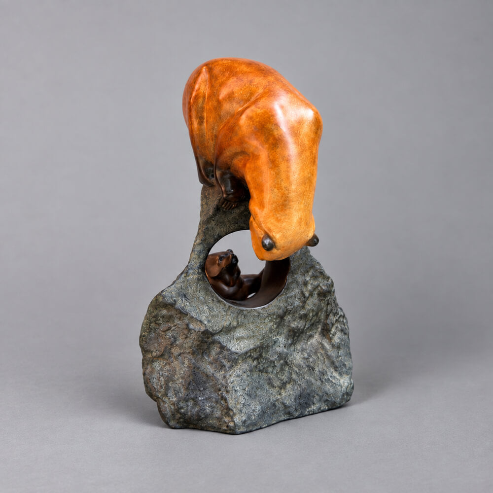 A bronze sculpture of two bears, one large bear climbing a tall bronze rock while a smaller bear stands below, photographed against a neutral grey studio background.