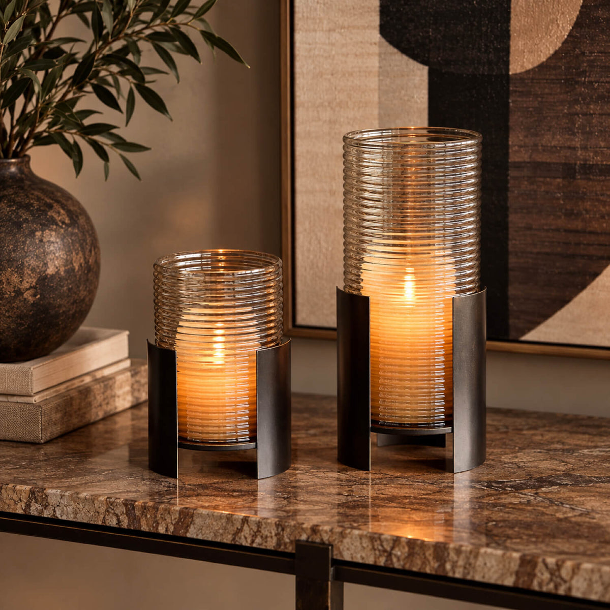 Smoked Gold Hurricane in small and large sizes, displayed together on a marble console with warm candlelight and a dark bronze frame