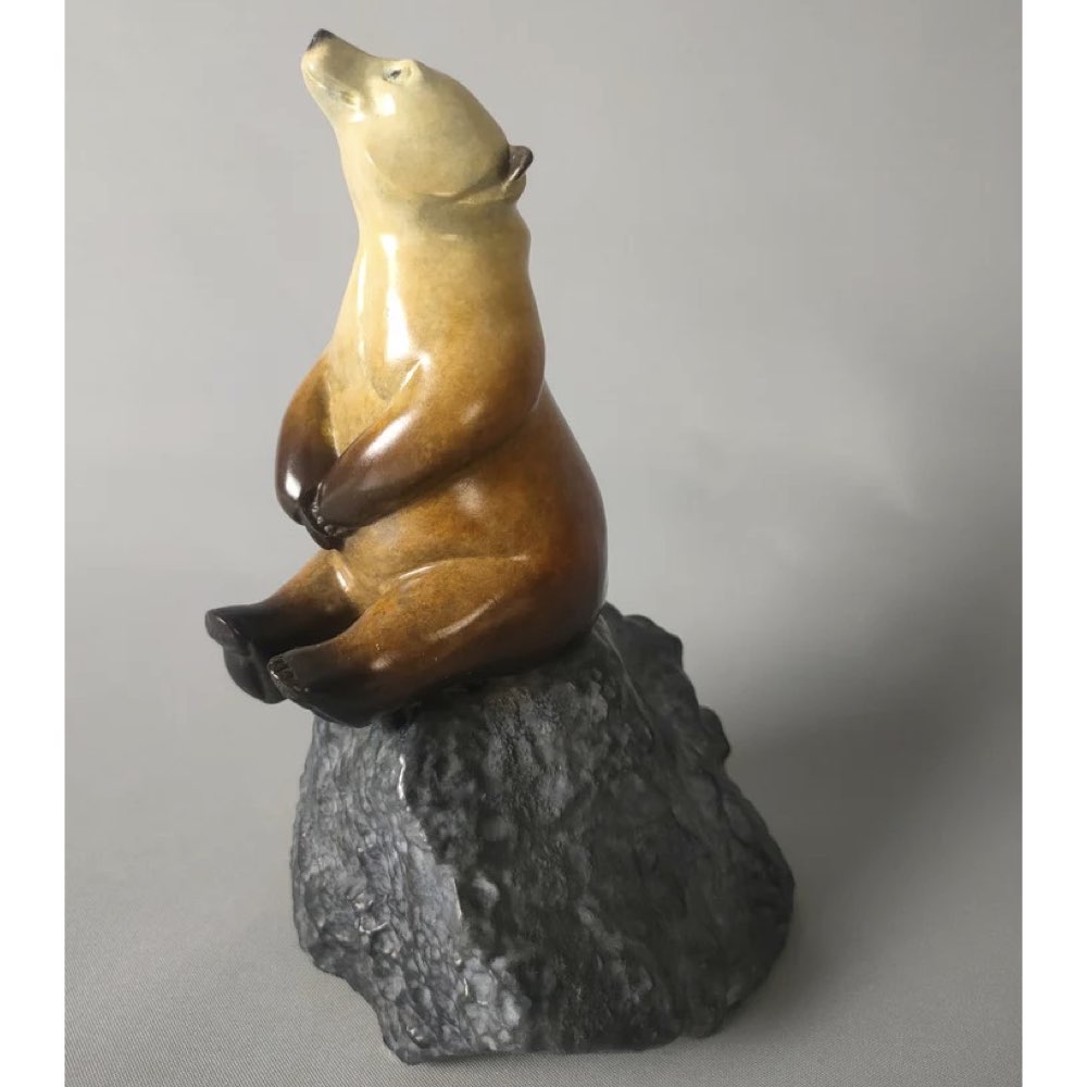 Bronze star gazing bear sculpture on a rock against a gray background