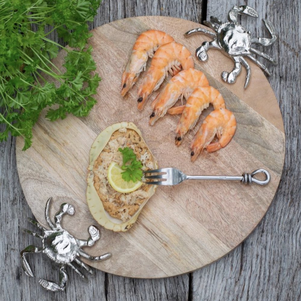 Wooden cutting board with prawns, a piece of bread with a lemon wedge, and a fork on a rustic wooden surface.