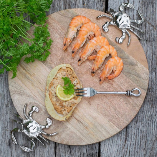 Wooden cutting board with prawns, a piece of bread with a lemon wedge, and a fork on a rustic wooden surface.