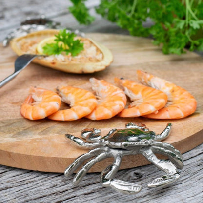 Shrimp on a wooden board with a crab-shaped handle in the foreground.